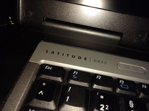Nahaufnahme der linken, oberen Ecke der Tastatur eines „Dell Latitude D830“-Laptops, so dass einige Tasten, der Schriftzug der Typbezeichnung und der untere Teil des Bildschirms zu sehen sind.